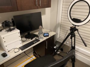 home office with ring light, computer, mouse, keyboard, and camera in view