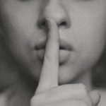 A person holding their finger over their mouth to indicate a secret